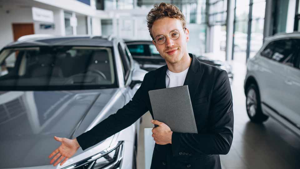 Ein Verkäufer zeigt auf ein Auto und erklärt dem Kunden die Konditionen beim Auto verkaufen Freiburg
